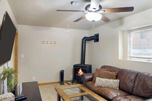 A living room with a fireplace, a ceiling fan, a TV, and a leather sofa. - Mountain Getaway • Hot Tub • Game Room • Sleeps 10 • Minutes to Payette Lake (McCall)