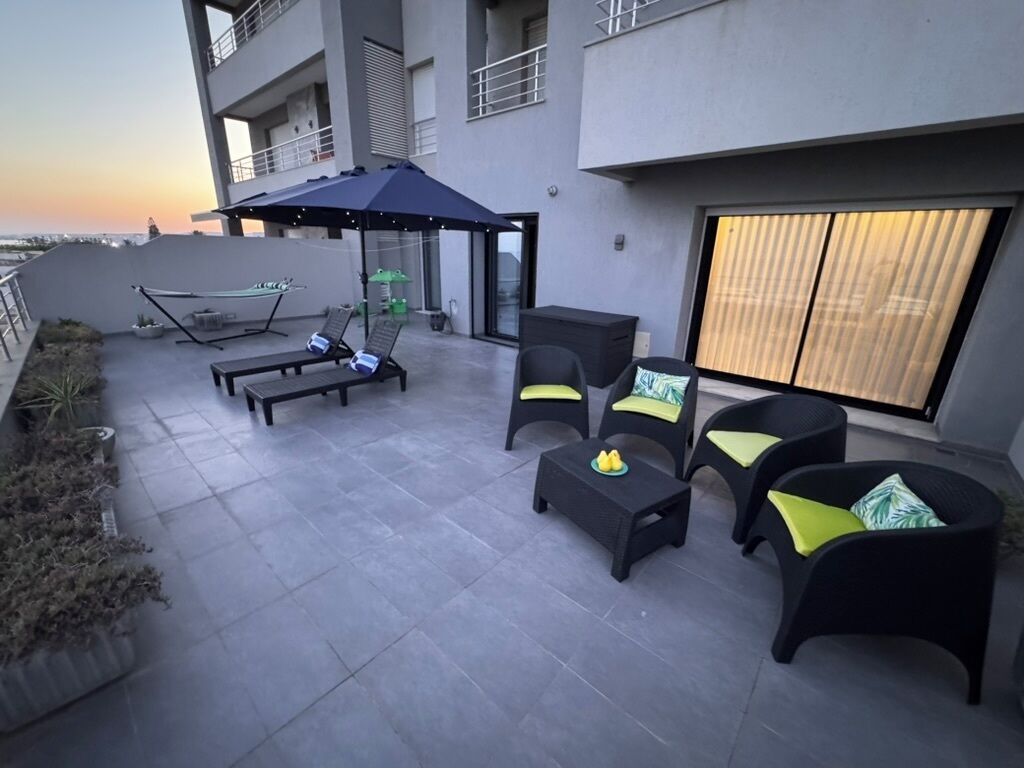 A rooftop patio with outdoor furniture, a hammock, and a view of the sunset.