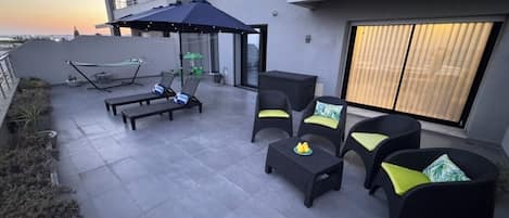 A rooftop patio with outdoor furniture, a hammock, and a view of the sunset.