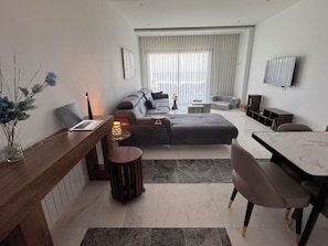 A modern living room with a sofa, a dining table, a TV mounted on the wall, and a laptop on a side table.