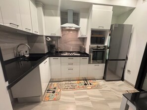 Una cocina moderna con gabinetes blancos, encimera negra, electrodomésticos de acero inoxidable y un tapete decorativo.