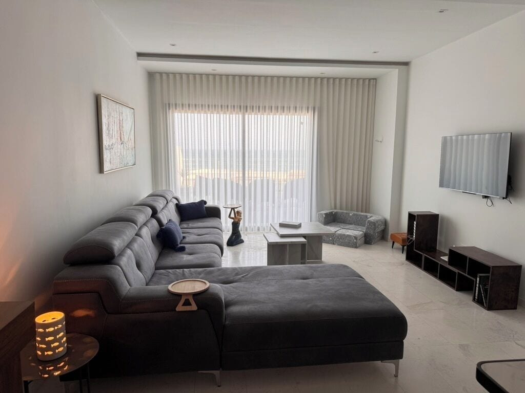 Ein modernes Wohnzimmer mit einer Couch, einem Hocker und einem an der Wand befestigten Flachbildfernseher.