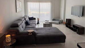 Moderni olohuone, jossa on sohva, rahi ja seinälle asennettu taulutelevisio.