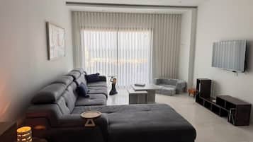 Ein modernes Wohnzimmer mit einer Couch, einem Hocker und einem an der Wand befestigten Flachbildfernseher.