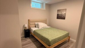 Une chambre à coucher avec un lit, une table de chevet, une lampe, une fenêtre et un tableau au mur.
