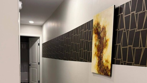 Un couloir doté d’un plancher en bois, une porte au fond et un mur orné de motifs géométriques et d’une seule œuvre d’art.