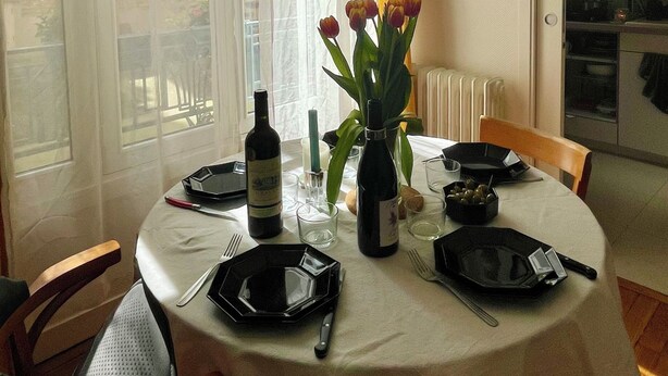 Ein Esstisch mit Geschirr, Besteck, einer Flasche und einer Blumenvase.