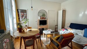 Ein kompakter Wohnbereich mit Essplatz, einem Bett, einem Fernseher und einer kleinen Arbeitsfläche.