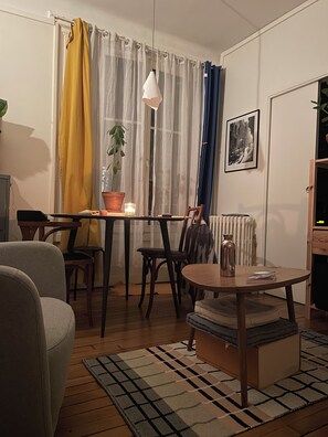 A cozy living room with a wooden floor, a round coffee table, a sofa, and a dining table. - Fully Equipped Apartment in La Bastille (Paris)