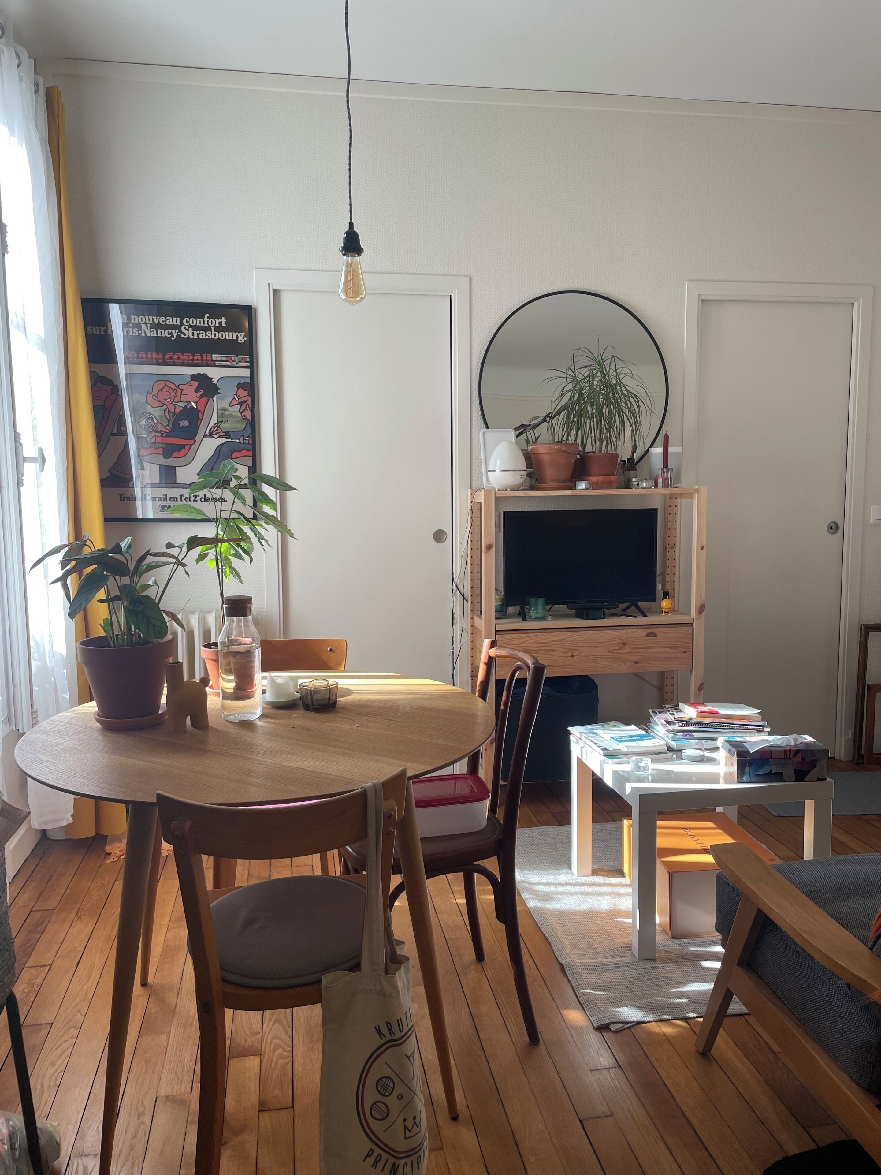 Ein gemütliches Wohnzimmer mit einem Holzesstisch, Stühlen, einem Fernseher auf einem Holzschrank und einer Topfpflanze.
