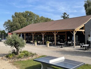An outdoor seating area with tables and chairs, a covered pavilion, and a ping pong table. - Camping Papillon Kinrooi - Pipowagen 4 p. terras by Interhome (Kinrooi)