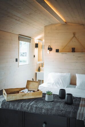 A cozy bedroom with a wooden ceiling, a bed with white bedding, a small plant, and two black vases on the nightstand. - Camping Papillon Kinrooi - Pipowagen 4 p. terras by Interhome (Kinrooi)