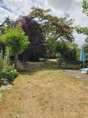 A fenced garden area with a variety of trees and a blue umbrella. - A charming, quiet, and rustic little cottage with a small garden and private parking. (Clisson)