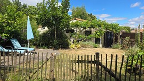 Ein umzäunter Garten mit Holzparkanlage, einem blauen Sonnenschirm und einem Haus mit einem Ziegeldach.