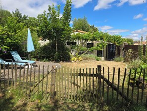 A fenced backyard with a wooden fence, a blue umbrella, and a house with a tiled roof. - A charming, quiet, and rustic little cottage with a small garden and private parking. (Clisson)