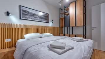 Quarto de hotel moderno com uma cama grande, cabeceira de madeira, um quadro pendurado, estantes embutidas e uma mesa de cabeceira.