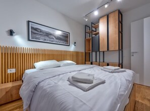 Een moderne hotelkamer met een groot bed, een houten hoofdbord, een wanddecoratie, ingebouwde planken en een nachtkastje.