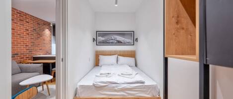 A compact bedroom with a bed, a small table, a sofa, and a brick wall.