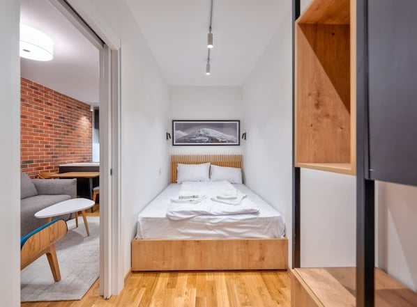 Un dormitorio pequeño con cama, una mesita, un sofá y una pared de ladrillo.