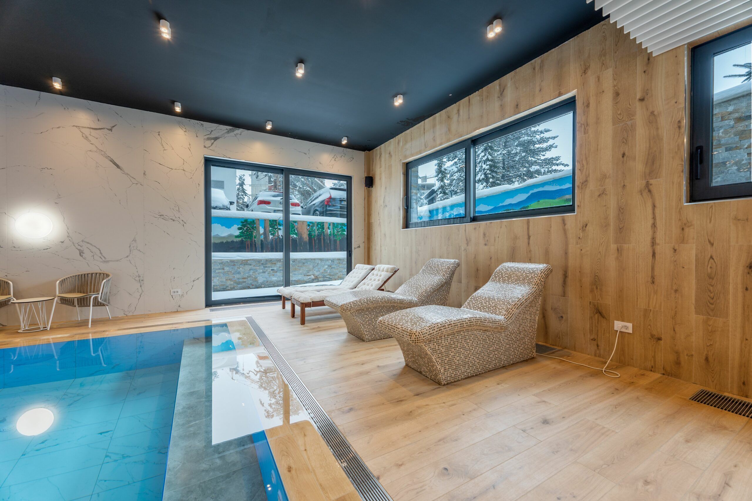 Un interior moderno con piscina, sillones de mimbre y grandes ventanales con vistas nevadas.