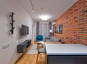 Una sala de estar moderna con pared de ladrillo, un televisor de pantalla plana, un sofá, una mesa de comedor y una silla azul.