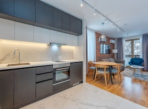 Una cocina moderna con encimera de mármol, horno integrado y muebles oscuros.