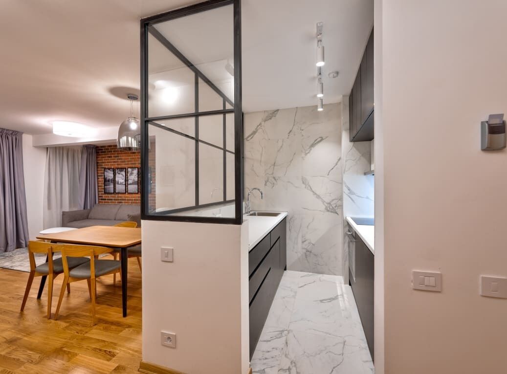Une cuisine moderne dotée de plans de travail en marbre, d’un four encastré et d’un coin repas avec une table et des chaises en bois.