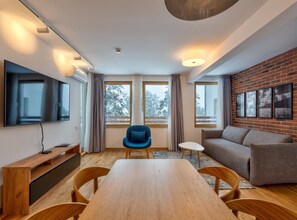 Een moderne woonkamer met een houten eettafel, een blauwe stoel, een grijze bank en een flatscreen televisie aan de muur.