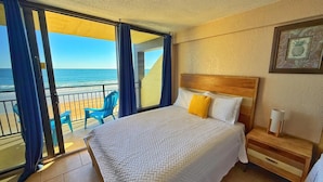 Quarto de hotel com cama, mesa de cabeceira, cadeira e vista para a praia.