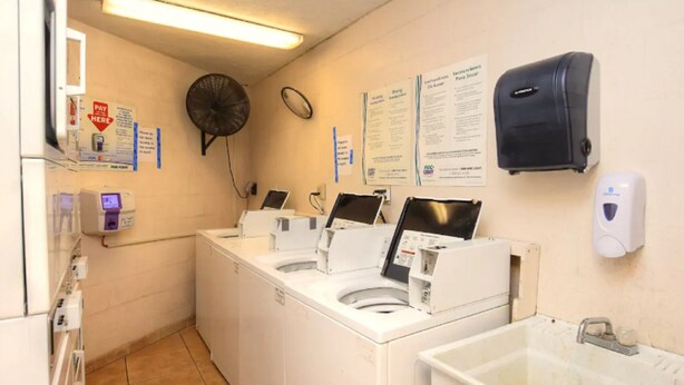 Uma lavanderia com várias máquinas de lavar, um ventilador, um dispensador de papel e um dispensador de sabonete líquido.