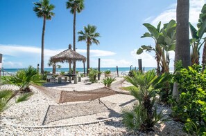A beach area with a thatched gazebo, palm trees, and a pebble path leading to the sea. - NEW Amazing Ocean Front Retreat in Daytona Beach! (Daytona Beach Shores)