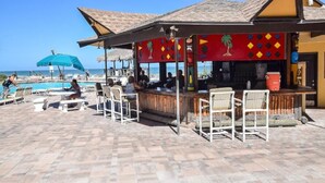 Um bar à beira-mar com mesas ao ar livre e uma piscina ao fundo.