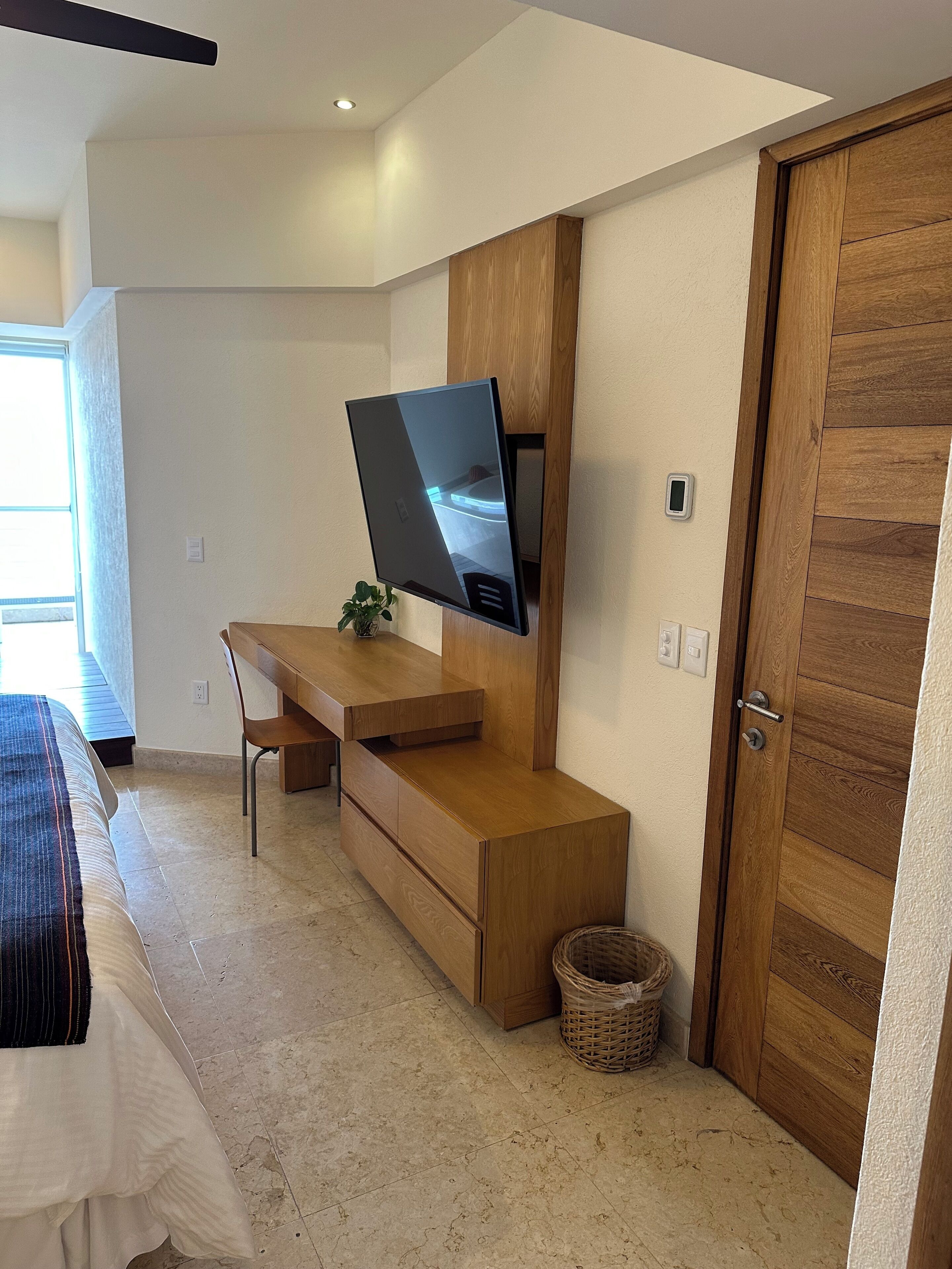 A modern bedroom with a bed, a desk, a TV, a door, and a window.