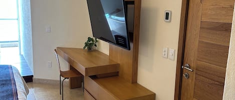 A modern bedroom with a bed, a desk, a TV, a door, and a window.