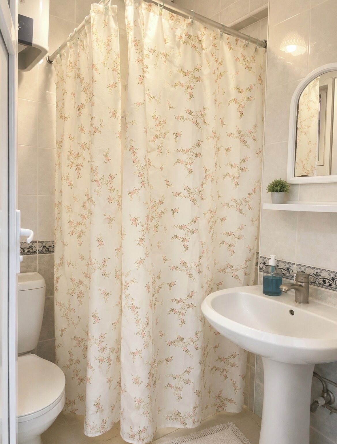 Et badeværelse med badeforhæng, toilet, vask og en lille plantepotte.