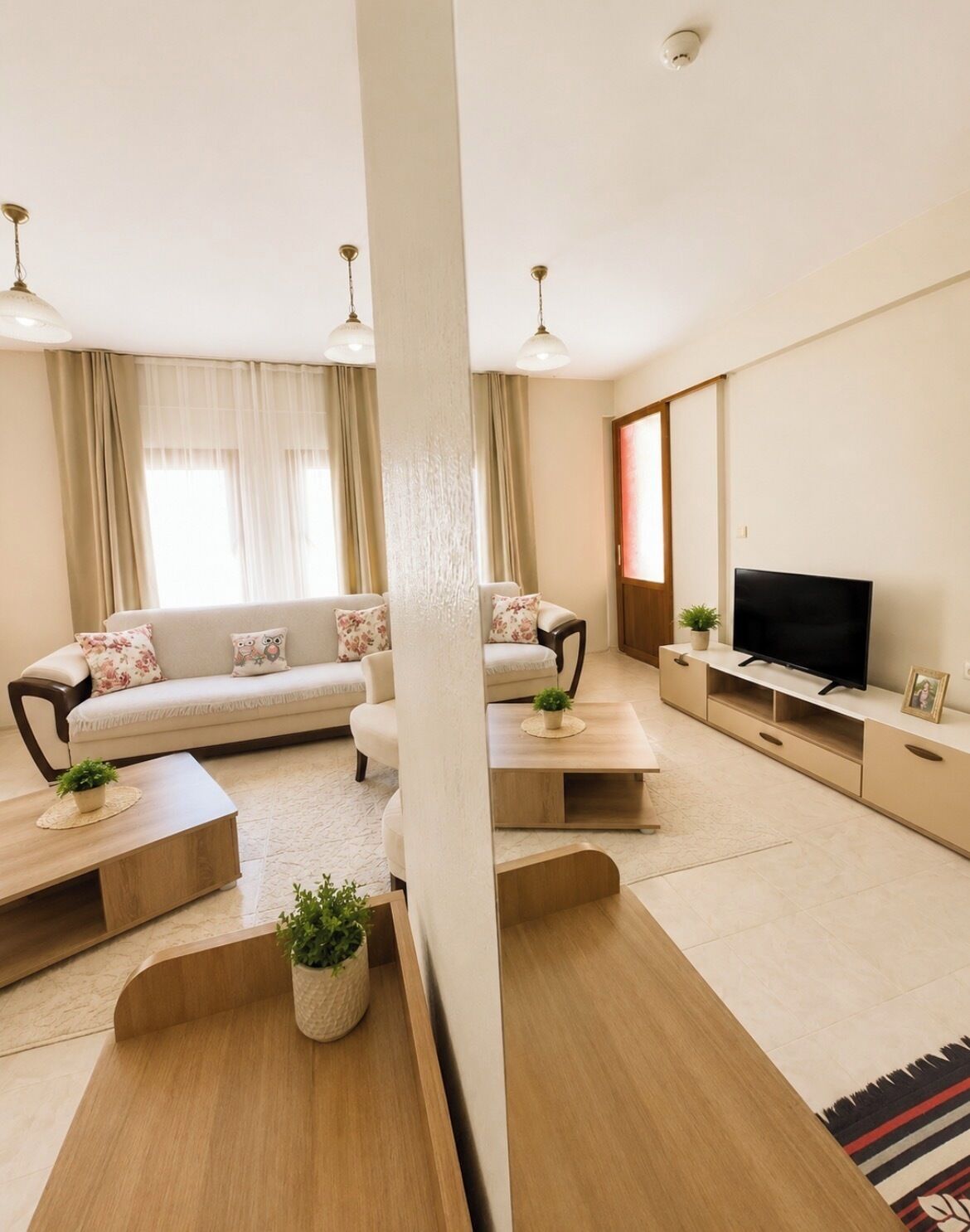 A modern living room with a sofa set, a flat-screen TV, and wooden coffee tables.