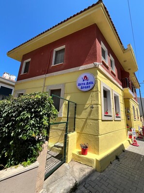 A two-story building with a yellow facade and a red roof. There is a sign on the front that reads 'ASYA ASIL APART'.