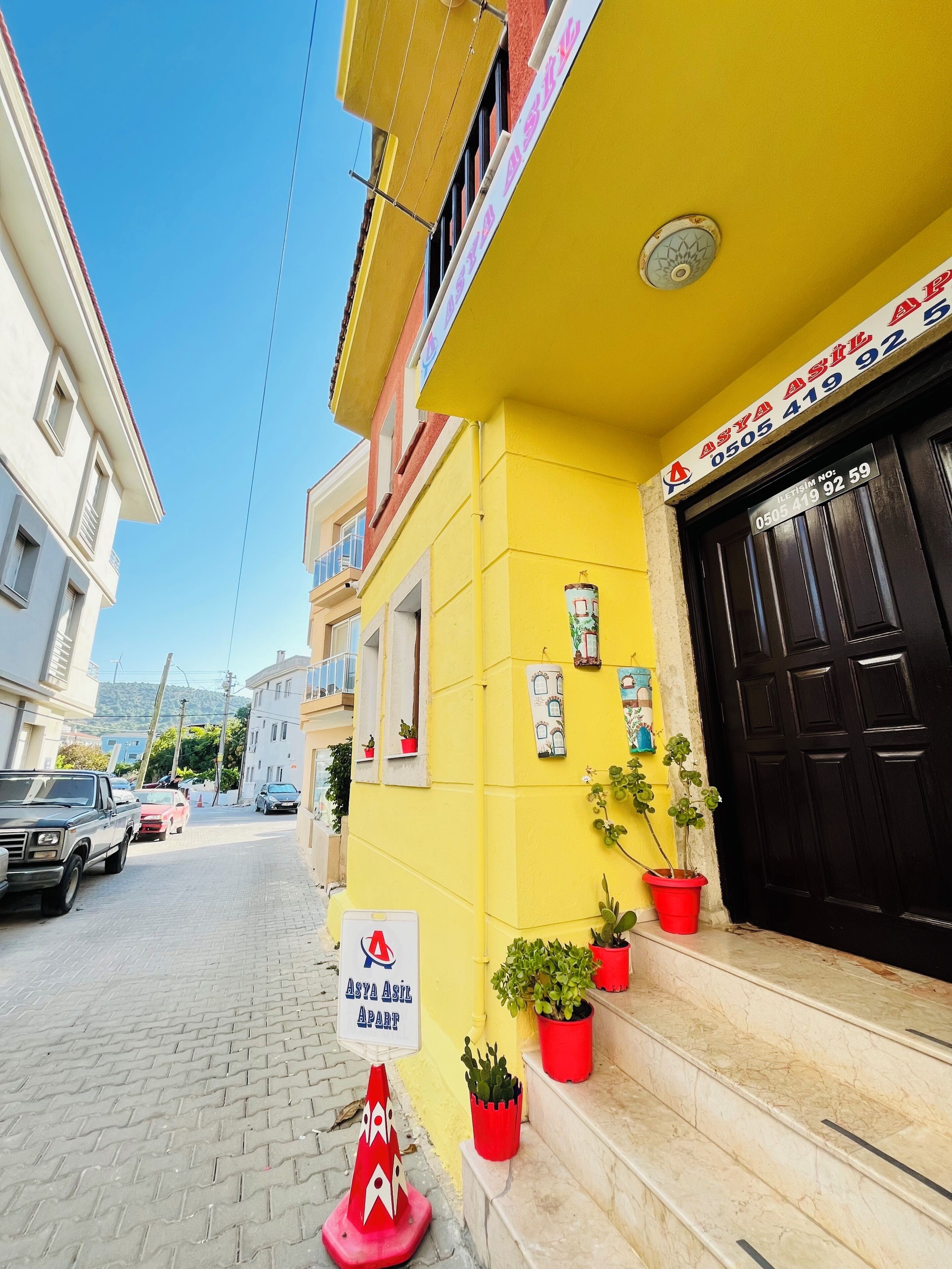 Un edificio amarillo con puerta negra, plantas en macetas y un letrero que indica que es un apartamento.