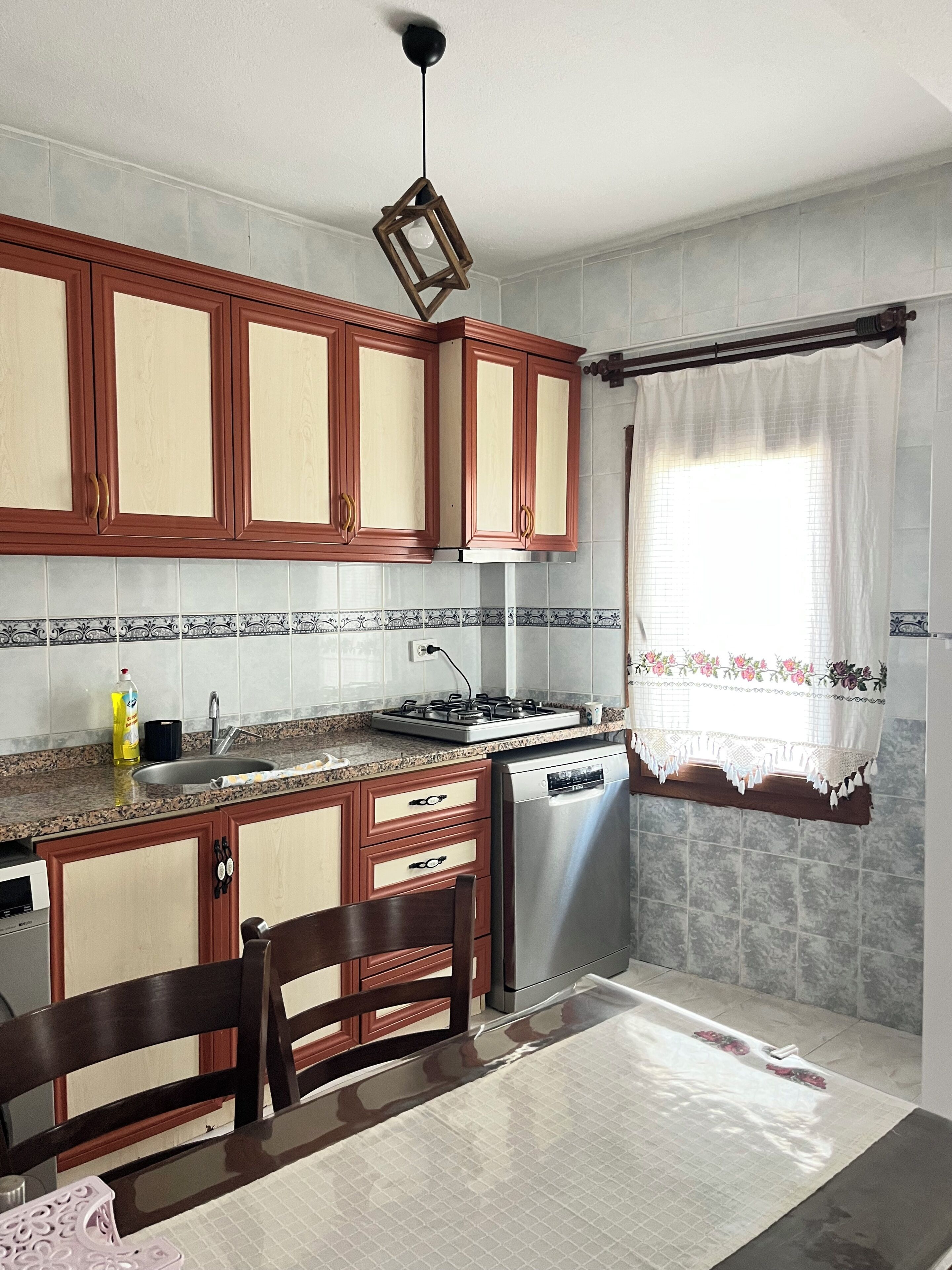 A kitchen with wooden cabinets, a gas stove, a dishwasher, and a window with curtains.