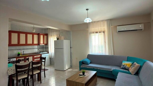 A living room with a sofa, a coffee table, a dining area with chairs, and a kitchen with cabinets and a refrigerator.