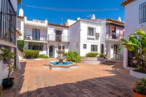 A courtyard with a fountain, potted plants, and white buildings with balconies. - Holiday Home in Nerja With Sea Views & Pool (Nerja)
