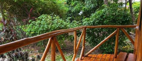 Eine Holzterrasse mit Geländer, umgeben von üppiger Vegetation und verschiedenen Pflanzen.