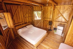 A wooden cabin bedroom with a bed, a small refrigerator, and a window.