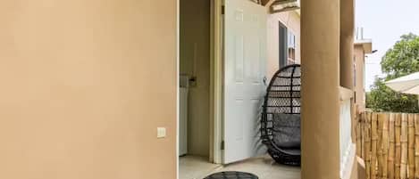 Un pasillo que conduce a una habitación con una puerta, una silla y una valla de bambú.