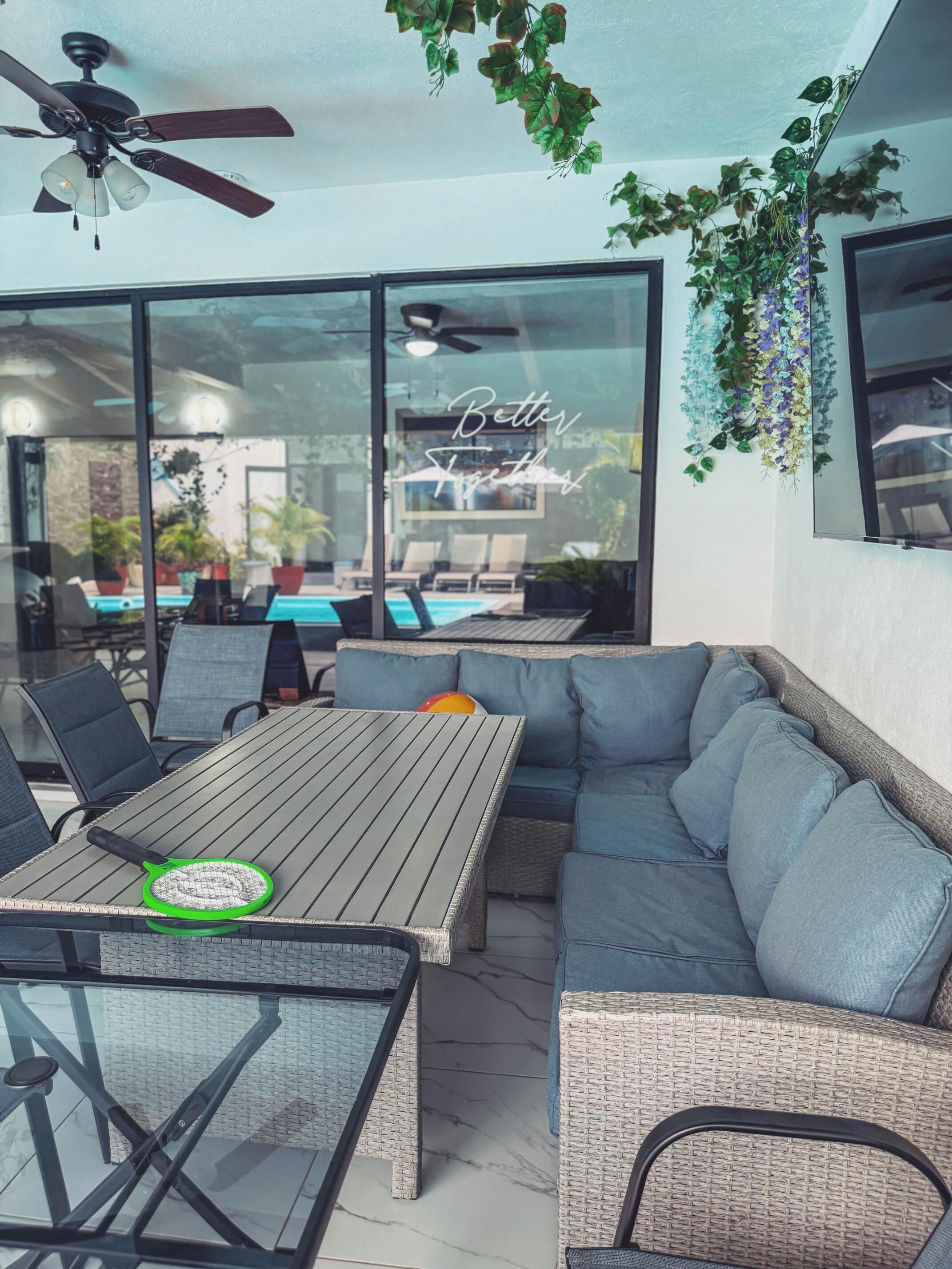 A modern outdoor seating area with a glass wall, a ceiling fan, and a pool view.