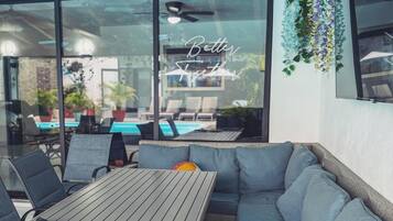 A modern outdoor seating area with a glass wall, a ceiling fan, and a pool view.