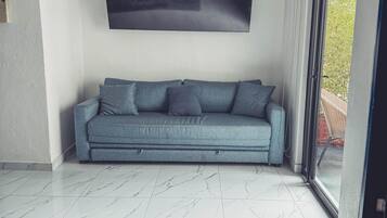 A modern living room with a sofa, a flat-screen TV, and a large window.