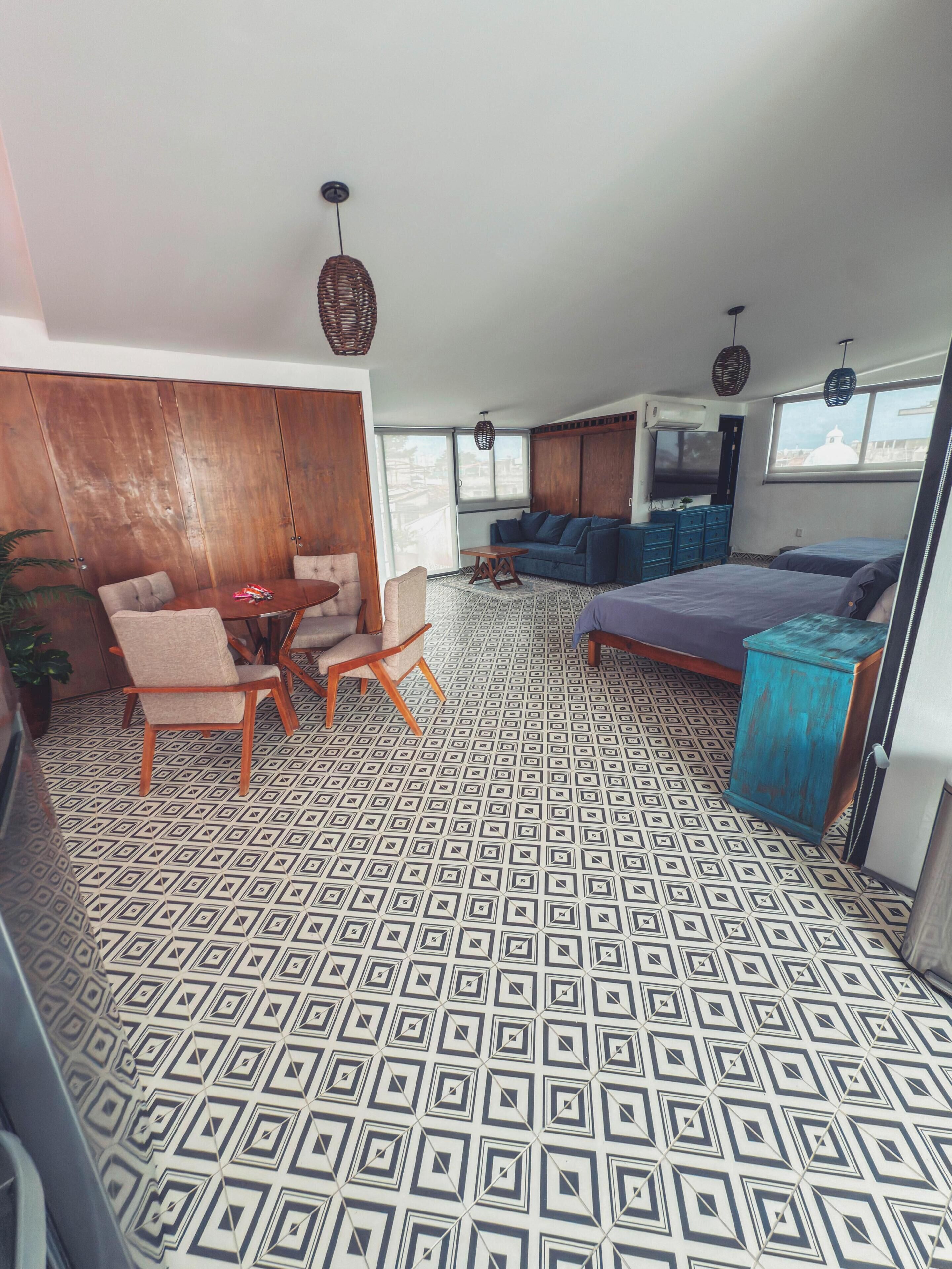 Una habitación amplia con suelo estampado, un sofá, una cama y una zona de comedor con sillas.