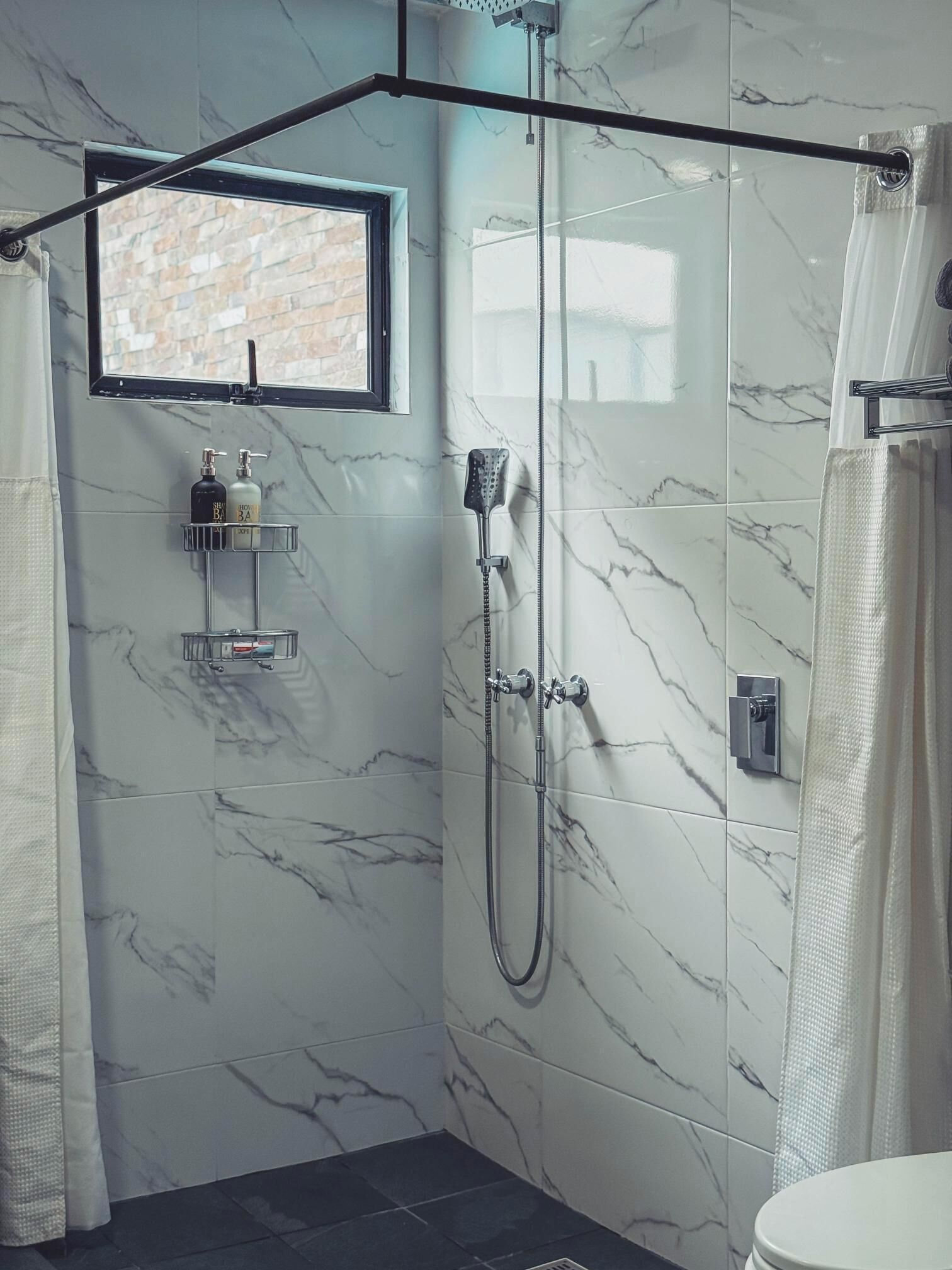 Un baño con ducha, ventana y toallero.