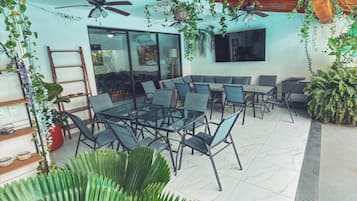 Un patio al aire libre con comedor, ventiladores de techo y abundante vegetación.